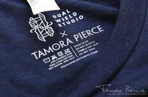 Closeup of printed-on Dual Wield Studio x Tamora Pierce tag with garment care below.