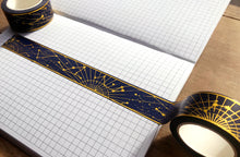Load image into Gallery viewer, Gold foil constellation washi tape over gridded journal page on wooden table.