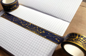 Gold foil constellation washi tape over gridded journal page on wooden table.