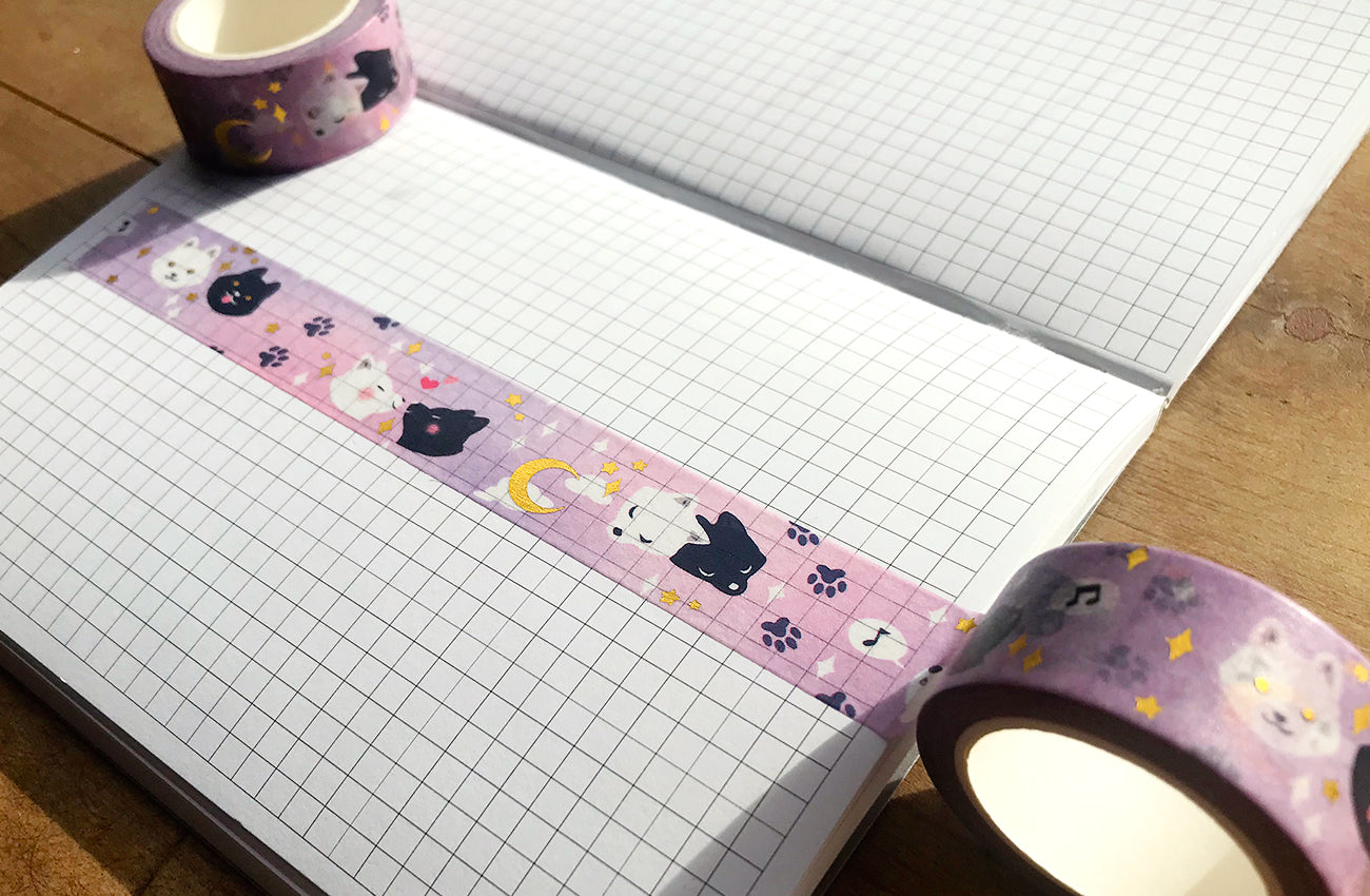 Unrolled celestial wolves washi tape onto a gridded journal page on a wooden table.