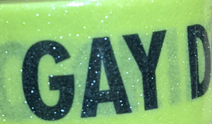 Detail of sparkly yellow, caution-tape inspired washi tape with black "BE GAY DO CRIMES" text on white background