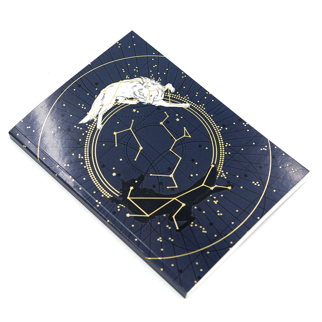 Soft cover journal depicting a navy star chart with a white wolf and a black wolf circling one another. White background.